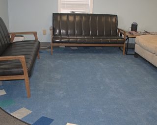 Three couches and a small side table arranged around a blue rug in a waiting room with light blue walls.