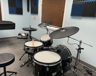 A black drum set with cymbals and practice pad in a carpeted music room with acoustic foam on the walls.