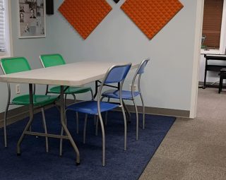 A rectangular table with four chairs on a blue rug in a room with soundproof foam panels and photos on the wall.